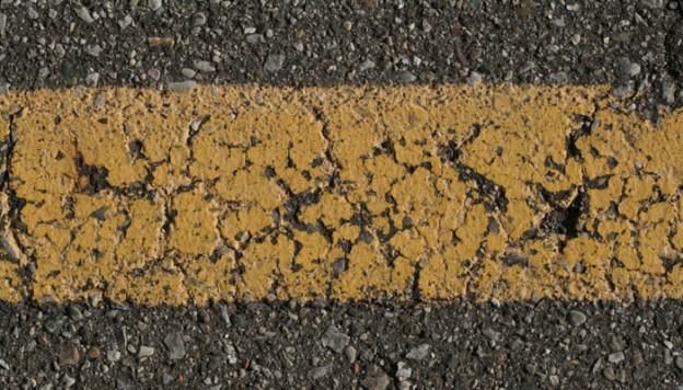 photo of cracked, yellow paint strip on asphalt.